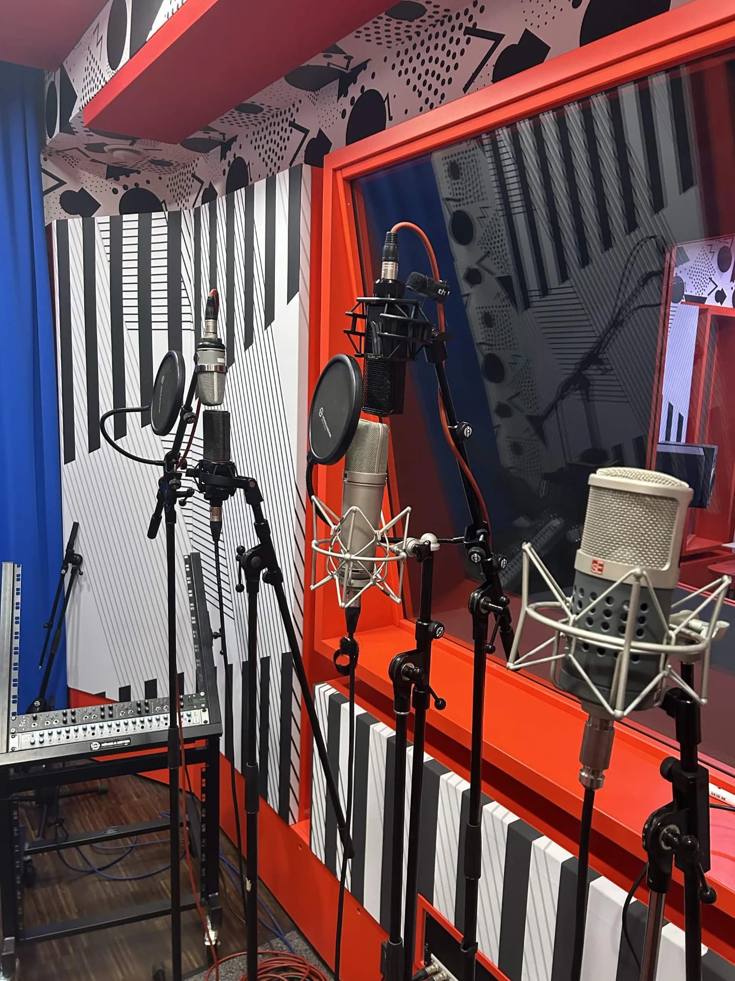 Condenser microphones on stands with pop filters in a colourful recording booth